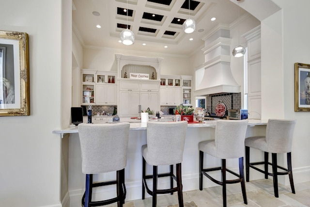 kitchen featuring white cabinetry, a breakfast bar, pendant lighting, and coffered ceiling