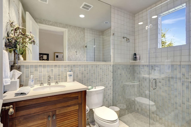 bathroom with a shower with door, vanity, tile walls, and toilet