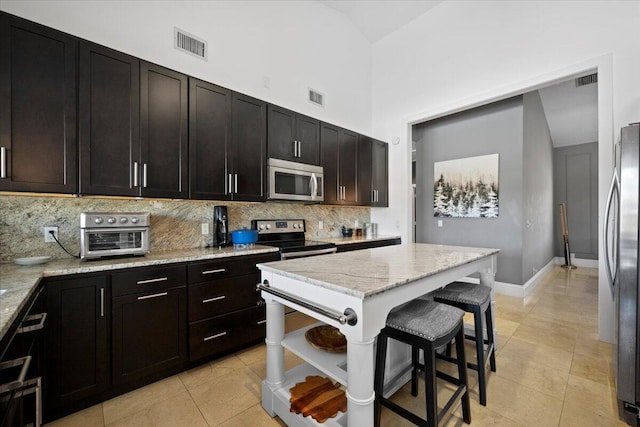 kitchen with appliances with stainless steel finishes, high vaulted ceiling, light tile patterned flooring, light stone countertops, and dark brown cabinetry