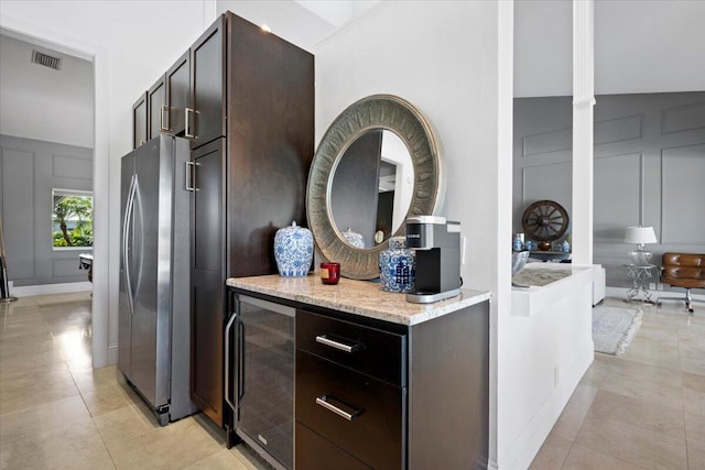 kitchen featuring wine cooler, light tile patterned flooring, dark brown cabinetry, stainless steel fridge, and light stone counters