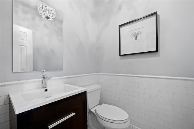 bathroom featuring toilet, tile walls, vanity, and a notable chandelier