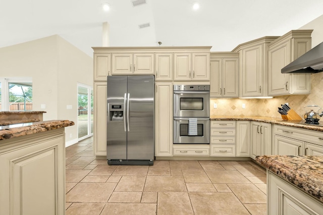 kitchen featuring light stone countertops, cream cabinets, wall chimney exhaust hood, stainless steel appliances, and decorative backsplash