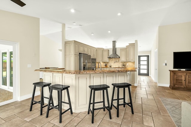 kitchen featuring a large island, light stone counters, cream cabinets, wall chimney exhaust hood, and appliances with stainless steel finishes