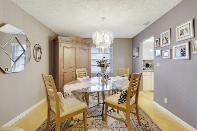 dining space featuring a textured ceiling, light hardwood / wood-style floors, and an inviting chandelier