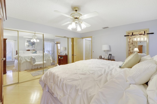 bedroom featuring ceiling fan, light hardwood / wood-style floors, a textured ceiling, and two closets