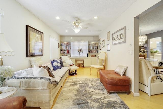 living room featuring ceiling fan with notable chandelier, a textured ceiling, and light hardwood / wood-style flooring