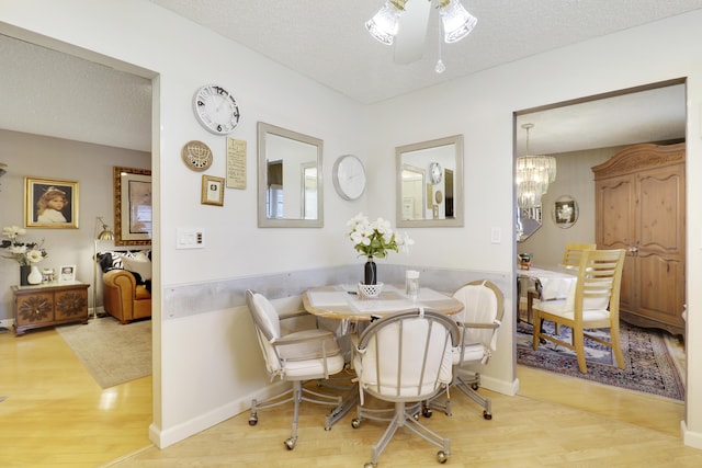 dining area with ceiling fan with notable chandelier, wood-type flooring, and a textured ceiling