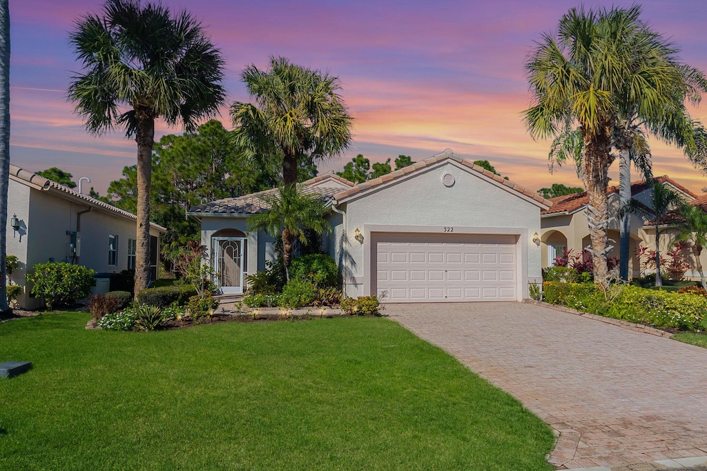 mediterranean / spanish house with a garage, stucco siding, a tile roof, a front lawn, and driveway