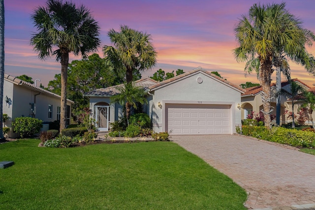 mediterranean / spanish house with a garage, stucco siding, a tile roof, a front lawn, and driveway