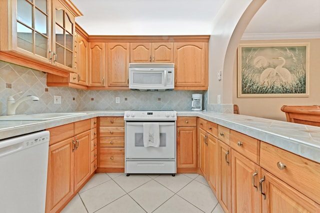 kitchen with light tile patterned flooring, white appliances, a sink, decorative backsplash, and glass insert cabinets