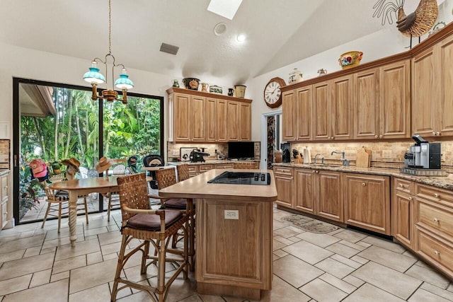 kitchen with tasteful backsplash, decorative light fixtures, a kitchen island, vaulted ceiling with skylight, and black stovetop