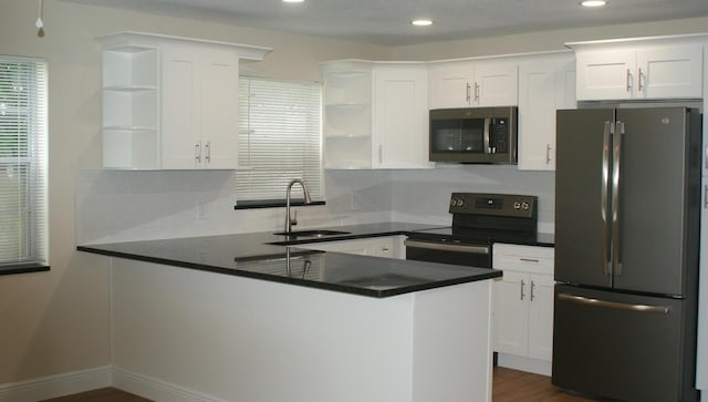 kitchen with electric range, white cabinetry, kitchen peninsula, and stainless steel refrigerator