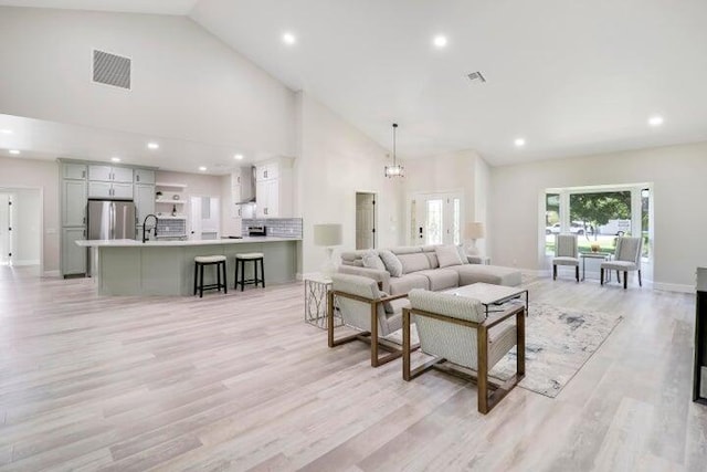 living room with light hardwood / wood-style flooring, high vaulted ceiling, a chandelier, and sink