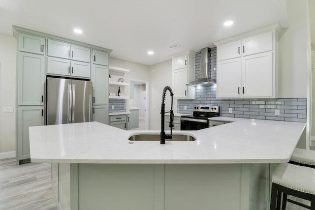 kitchen featuring decorative backsplash, appliances with stainless steel finishes, wall chimney exhaust hood, a breakfast bar, and sink