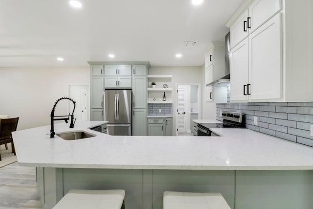 kitchen featuring kitchen peninsula, a breakfast bar, stainless steel appliances, wall chimney range hood, and sink