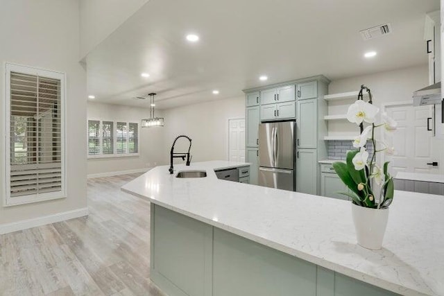 kitchen featuring sink, hanging light fixtures, light hardwood / wood-style flooring, light stone countertops, and appliances with stainless steel finishes