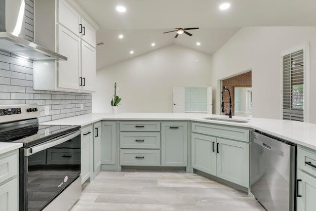 kitchen with sink, vaulted ceiling, wall chimney exhaust hood, appliances with stainless steel finishes, and tasteful backsplash