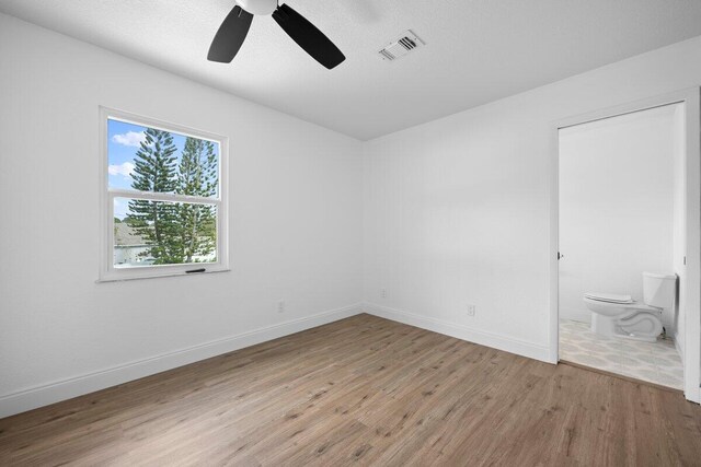 unfurnished bedroom featuring ceiling fan, light hardwood / wood-style floors, a textured ceiling, and two closets