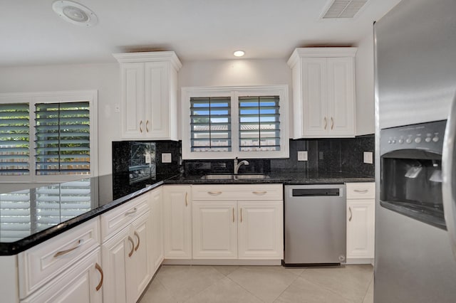 kitchen with appliances with stainless steel finishes, white cabinetry, dark stone counters, and sink