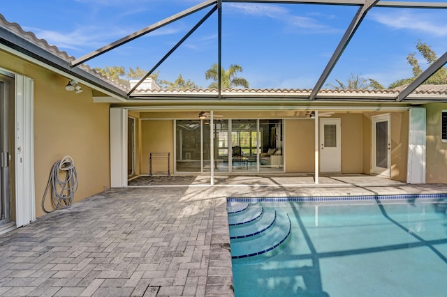 view of swimming pool with glass enclosure, ceiling fan, and a patio area