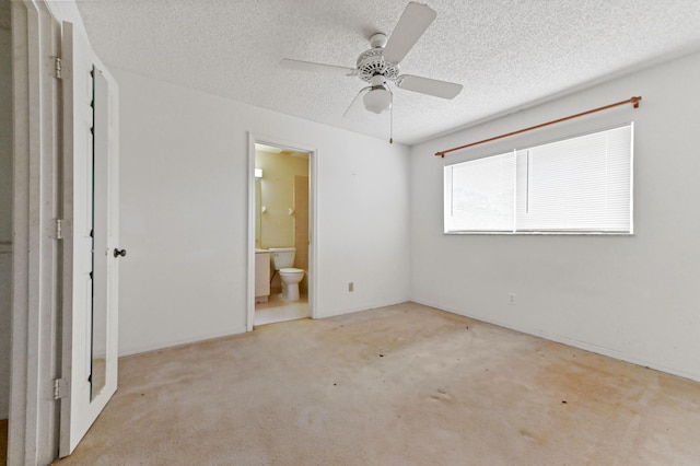 unfurnished bedroom with a textured ceiling, ceiling fan, light colored carpet, and ensuite bathroom