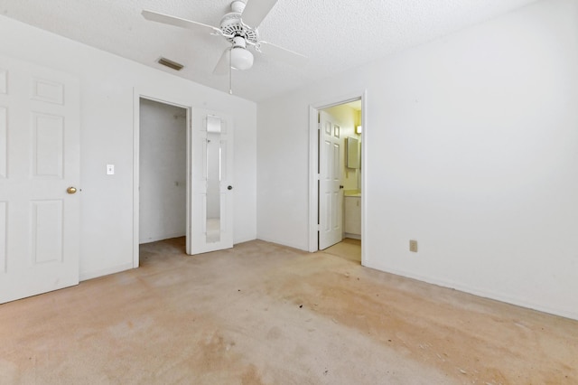 unfurnished bedroom with a textured ceiling, light colored carpet, ensuite bath, and ceiling fan