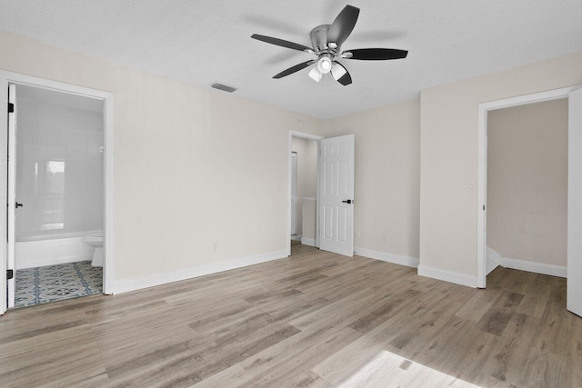 unfurnished bedroom featuring ceiling fan, a textured ceiling, connected bathroom, and light hardwood / wood-style flooring