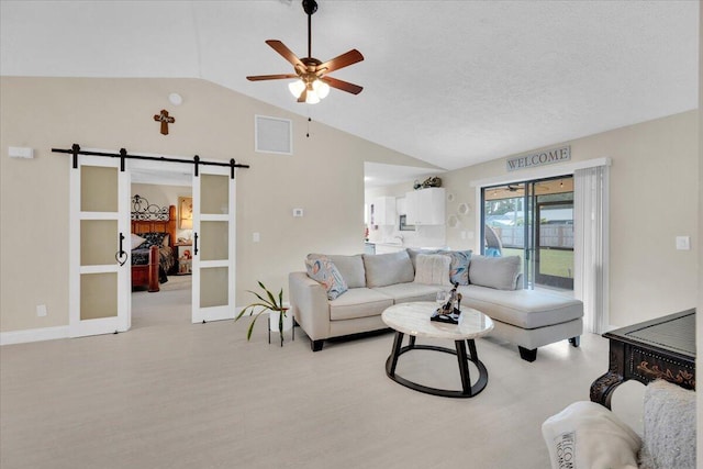 living room featuring a textured ceiling, vaulted ceiling, ceiling fan, a barn door, and light hardwood / wood-style floors