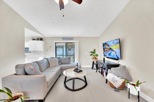 living room featuring ceiling fan, light wood-type flooring, a textured ceiling, and vaulted ceiling