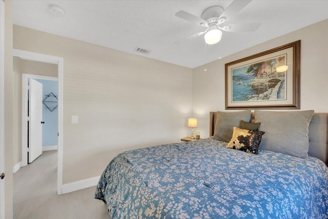 bedroom featuring a walk in closet, ceiling fan, light carpet, and a textured ceiling