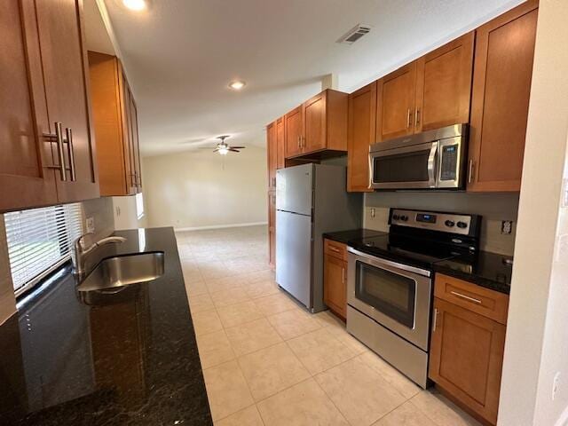 kitchen featuring stainless steel appliances, ceiling fan, dark stone counters, and sink