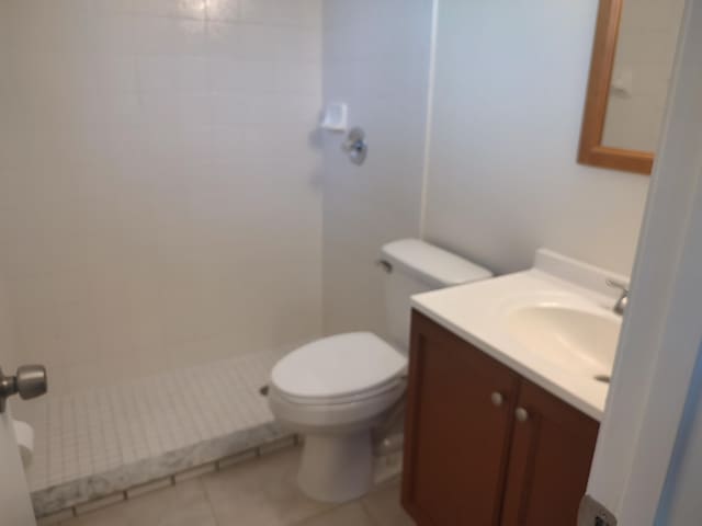 bathroom featuring tile patterned floors, toilet, a tile shower, and vanity