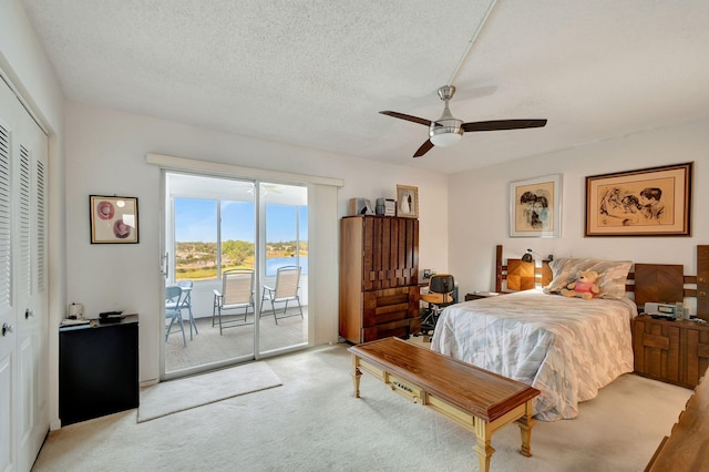 carpeted bedroom with access to outside, a water view, ceiling fan, a textured ceiling, and a closet