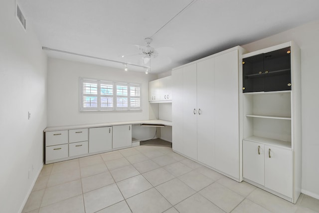 unfurnished office featuring ceiling fan, built in desk, rail lighting, and light tile patterned floors