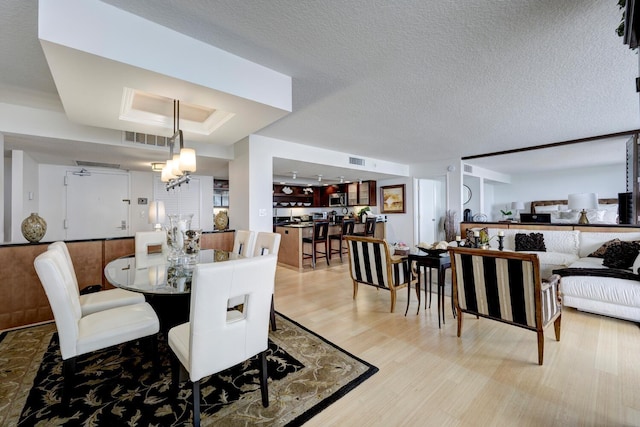 dining room featuring a tray ceiling, light hardwood / wood-style floors, a textured ceiling, and a notable chandelier