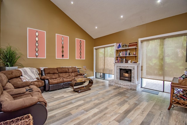 living room featuring a fireplace, light hardwood / wood-style flooring, high vaulted ceiling, and a textured ceiling