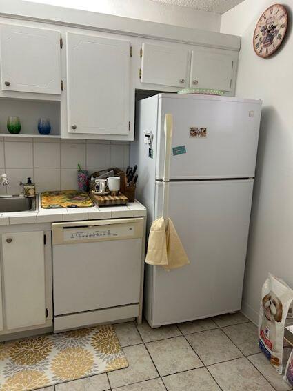 kitchen featuring white appliances, sink, decorative backsplash, light tile patterned floors, and white cabinetry