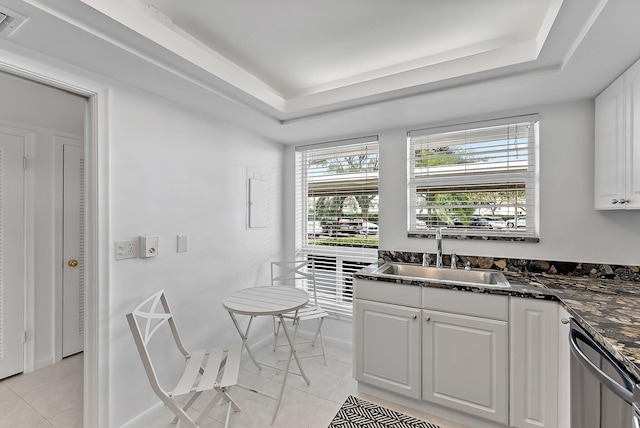 kitchen with white cabinetry, sink, stainless steel dishwasher, a tray ceiling, and light tile patterned flooring