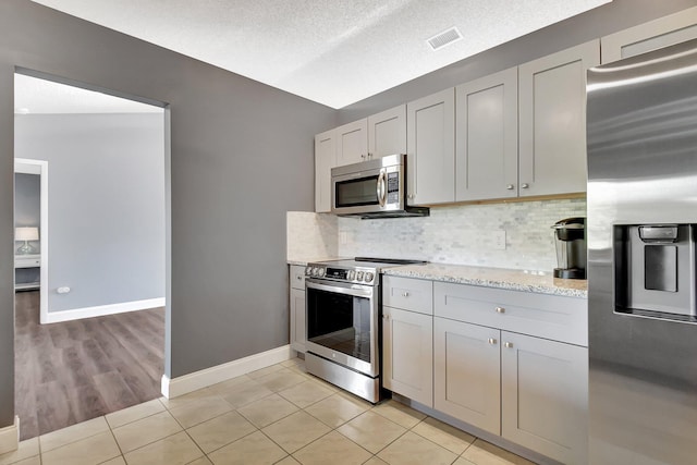 kitchen with a textured ceiling, decorative backsplash, stainless steel appliances, and vaulted ceiling