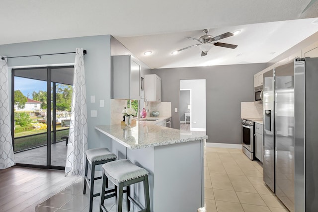 kitchen featuring sink, stainless steel appliances, light stone counters, kitchen peninsula, and light hardwood / wood-style floors