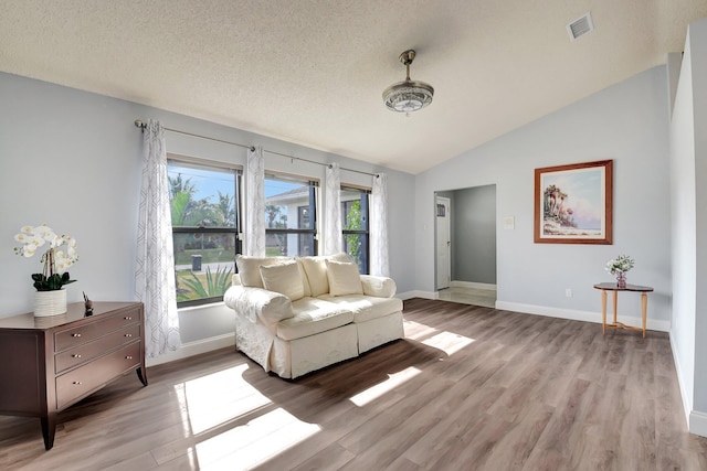 living room featuring a textured ceiling, light hardwood / wood-style floors, and lofted ceiling