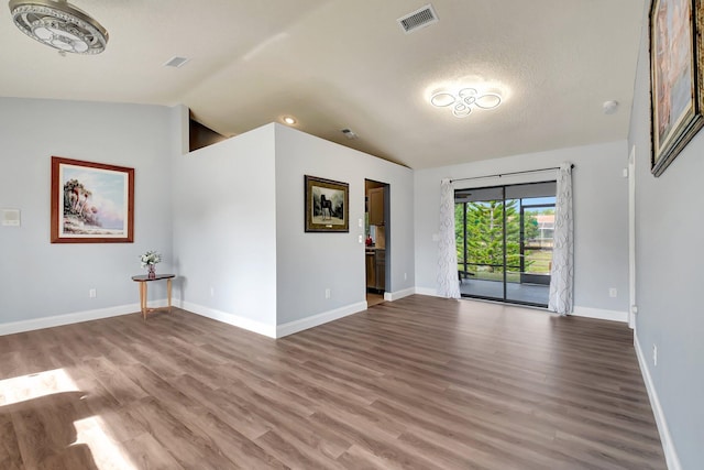 unfurnished room featuring a textured ceiling, wood-type flooring, and vaulted ceiling