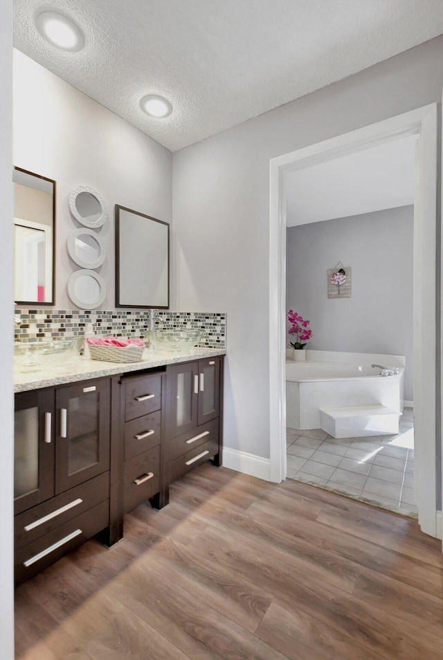 bathroom featuring a bath, backsplash, hardwood / wood-style floors, a textured ceiling, and vanity