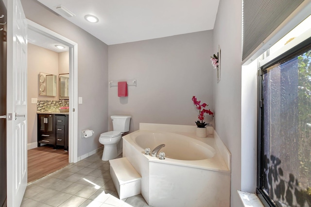 bathroom with vanity, tile patterned flooring, toilet, a tub to relax in, and tasteful backsplash