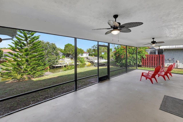 unfurnished sunroom featuring ceiling fan and a water view