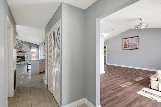 corridor with light hardwood / wood-style floors, an inviting chandelier, a textured ceiling, and vaulted ceiling