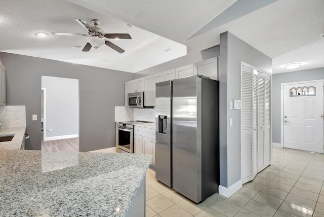 kitchen featuring appliances with stainless steel finishes, light stone counters, a textured ceiling, ceiling fan, and white cabinetry