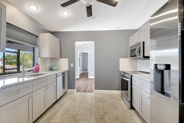 kitchen with decorative backsplash, appliances with stainless steel finishes, light stone counters, a textured ceiling, and light tile patterned floors