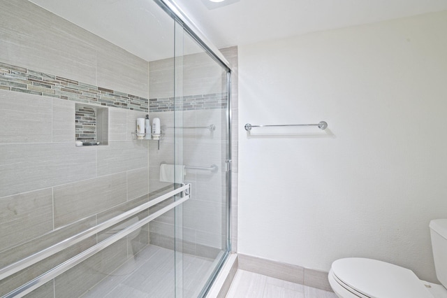 bathroom featuring tile patterned flooring, a shower with shower door, and toilet