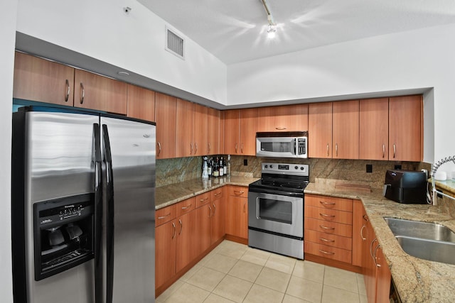 kitchen featuring decorative backsplash, appliances with stainless steel finishes, rail lighting, and light stone counters